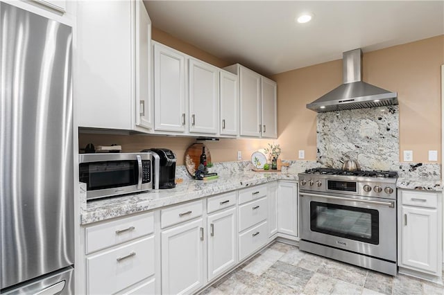 kitchen with stainless steel appliances, wall chimney range hood, white cabinets, light stone counters, and recessed lighting