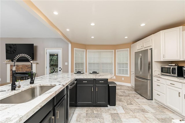 kitchen with appliances with stainless steel finishes, white cabinets, a sink, light stone counters, and recessed lighting