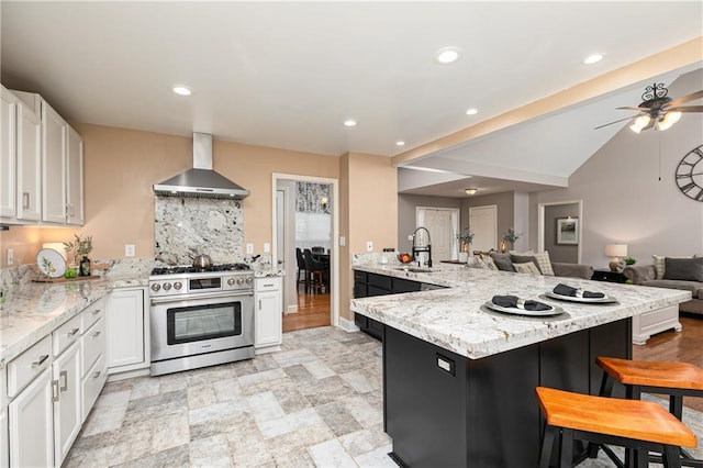 kitchen with wall chimney exhaust hood, stainless steel gas stove, a sink, a breakfast bar, and open floor plan