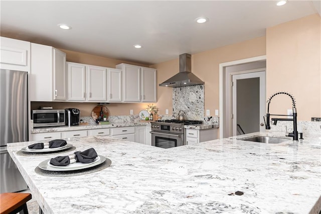 kitchen with wall chimney exhaust hood, appliances with stainless steel finishes, a sink, light stone countertops, and recessed lighting