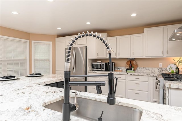 kitchen featuring stainless steel appliances, white cabinetry, recessed lighting, light stone counters, and wall chimney exhaust hood