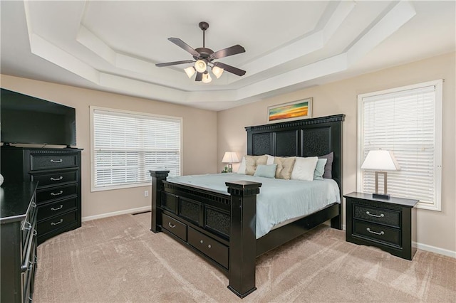 bedroom with a tray ceiling, baseboards, light carpet, and a ceiling fan