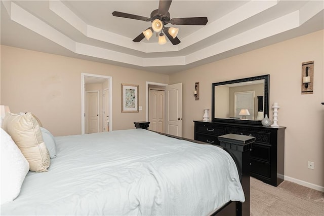 bedroom featuring a raised ceiling, light colored carpet, baseboards, and ceiling fan