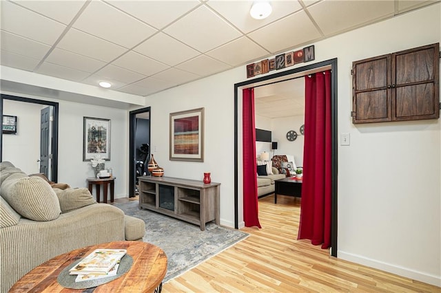 living room with a paneled ceiling, light wood-type flooring, and baseboards