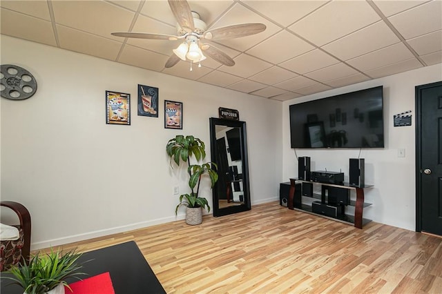 living area with light wood finished floors, a ceiling fan, a drop ceiling, and baseboards
