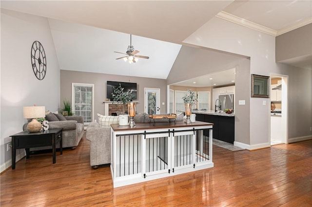 living area with a ceiling fan, light wood finished floors, baseboards, a fireplace, and high vaulted ceiling