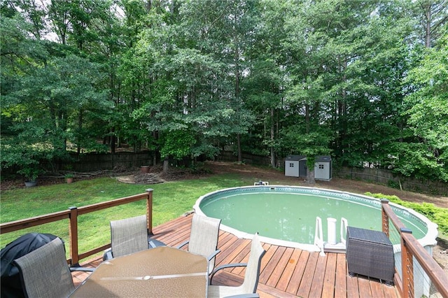outdoor pool featuring a wooden deck, outdoor dining area, a storage unit, an outdoor structure, and view of scattered trees