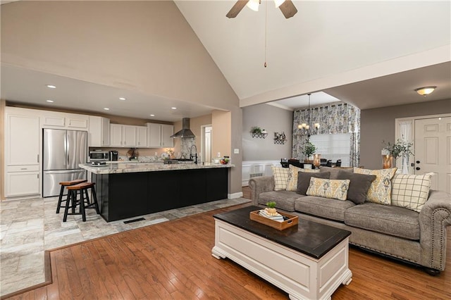 living area featuring light wood-style flooring, wainscoting, a chandelier, high vaulted ceiling, and a ceiling fan