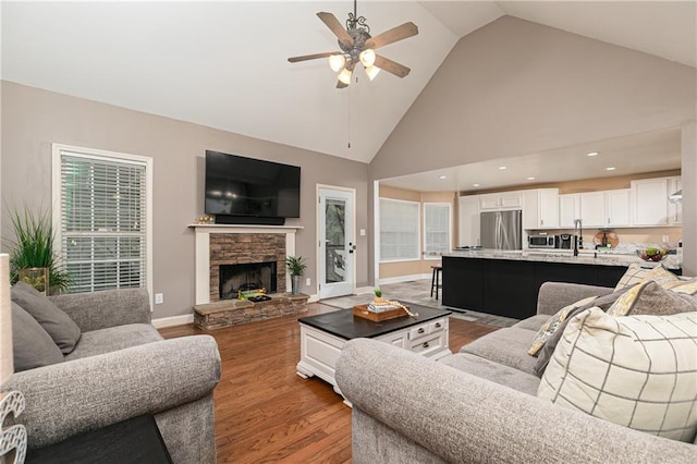 living room with ceiling fan, wood finished floors, high vaulted ceiling, a fireplace, and baseboards