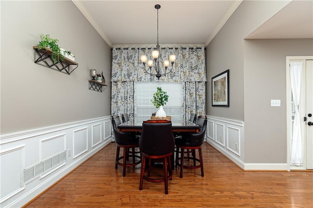 dining space featuring a chandelier, ornamental molding, a decorative wall, wood finished floors, and a wainscoted wall