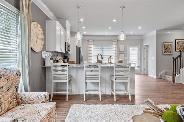 kitchen featuring stainless steel appliances, dark wood-type flooring, a kitchen breakfast bar, pendant lighting, and white cabinetry