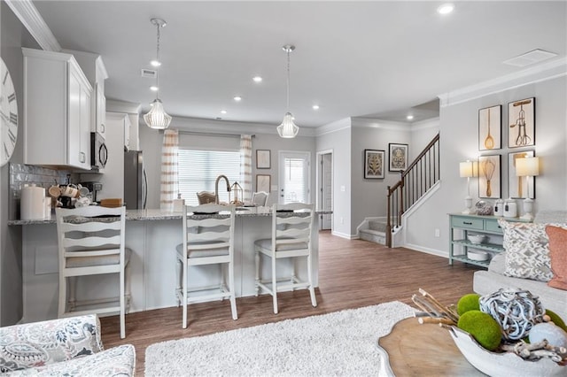 kitchen with crown molding, stainless steel appliances, white cabinetry, pendant lighting, and a breakfast bar