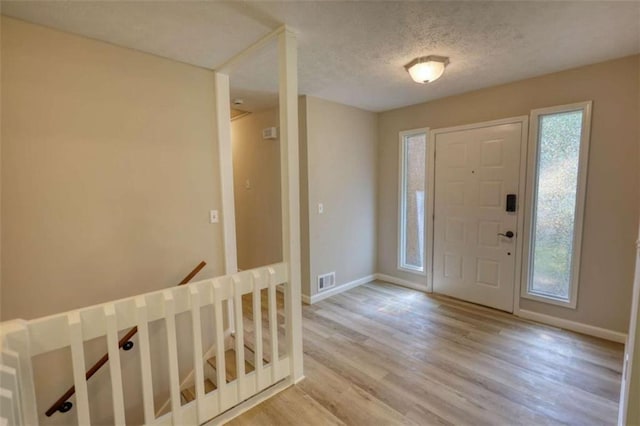 foyer with baseboards, visible vents, wood finished floors, and a textured ceiling