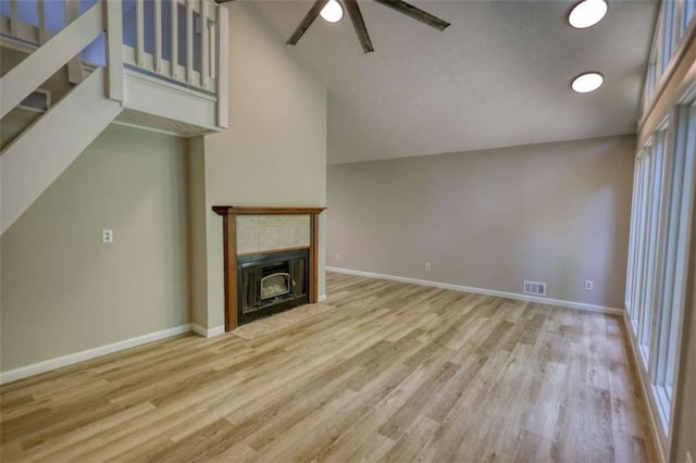 unfurnished living room featuring a fireplace with flush hearth, stairway, visible vents, wood finished floors, and a ceiling fan