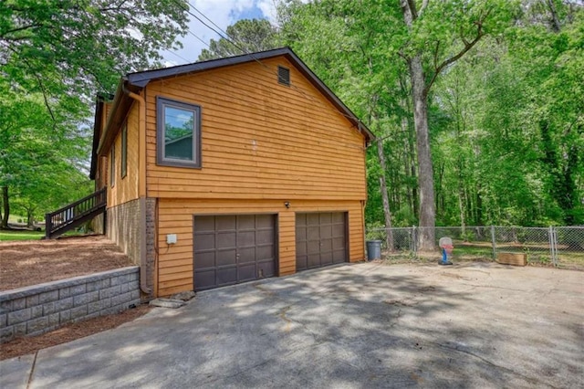 view of property exterior with a garage, fence, aphalt driveway, and stairs