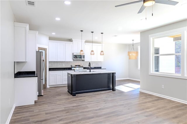 kitchen with white cabinetry, backsplash, hanging light fixtures, stainless steel appliances, and a center island with sink