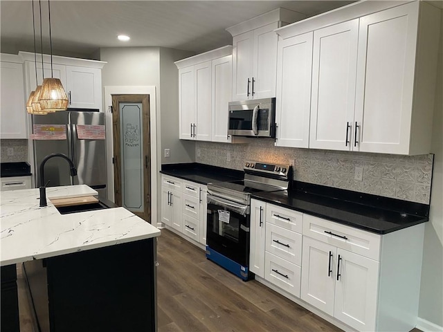 kitchen with decorative light fixtures, a center island with sink, dark stone countertops, appliances with stainless steel finishes, and white cabinets