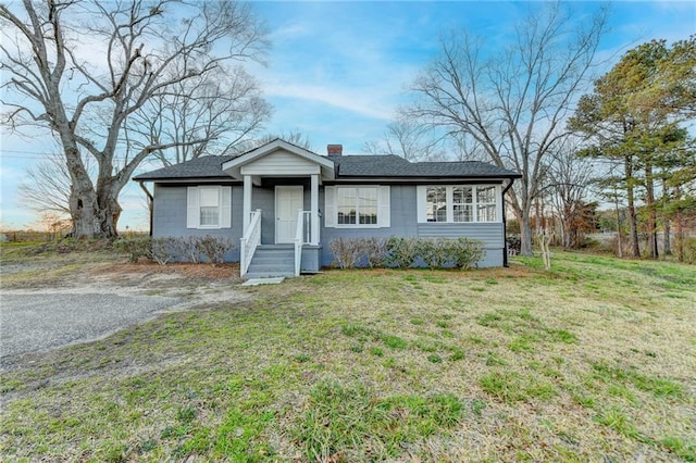 bungalow featuring a front lawn, roof with shingles, and a chimney