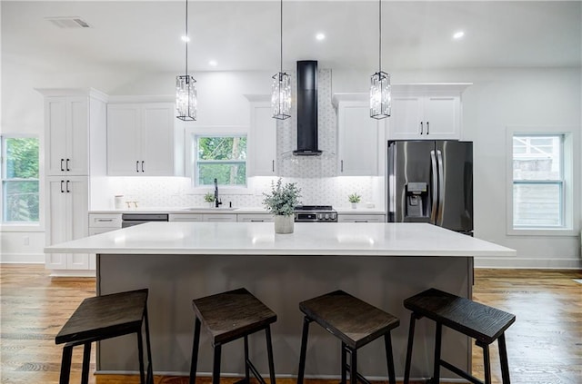 115 Dahlia Ave NW, Atlanta, GA 30314 - kitchen featuring stainless steel appliances, wall chimney range hood, a center island, white cabinets, and a kitchen breakfast bar