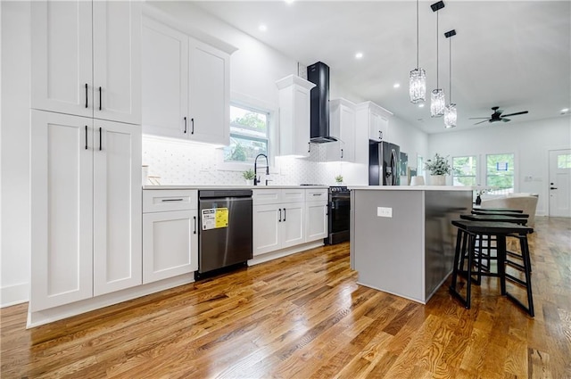 115 Dahlia Ave NW, Atlanta, GA 30314 - kitchen featuring appliances with stainless steel finishes, wall chimney exhaust hood, ceiling fan, light wood-style floors, and white cabinetry