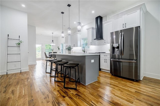 115 Dahlia Ave NW, Atlanta, GA 30314 - kitchen featuring stainless steel refrigerator with ice dispenser, wall chimney exhaust hood, a kitchen island, a breakfast bar area, and light wood finished floors