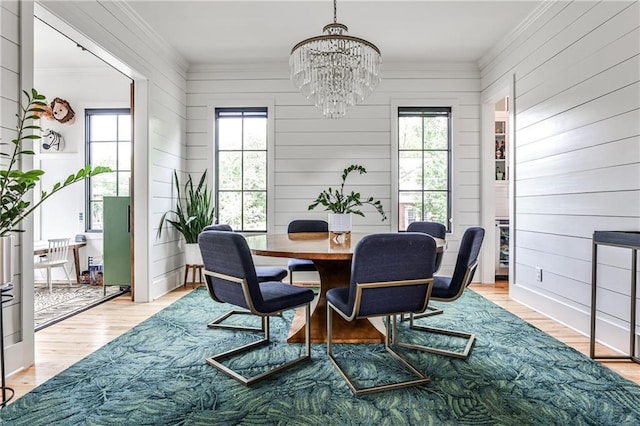dining area with an inviting chandelier, ornamental molding, light wood finished floors, and wood walls