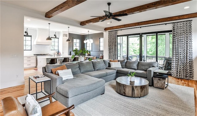living area featuring beamed ceiling, a wealth of natural light, ceiling fan with notable chandelier, and light wood-style floors