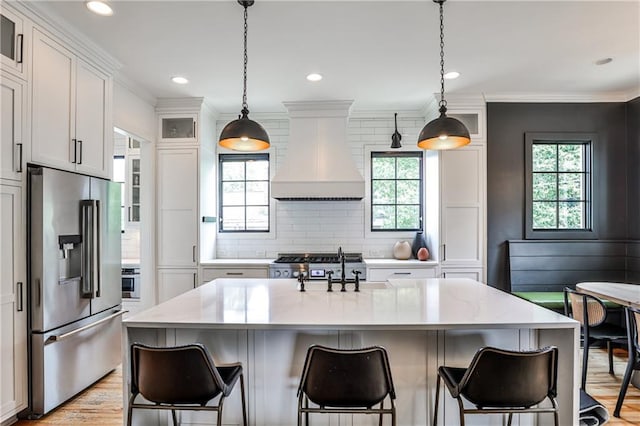 kitchen featuring a kitchen breakfast bar, white cabinets, tasteful backsplash, custom range hood, and appliances with stainless steel finishes