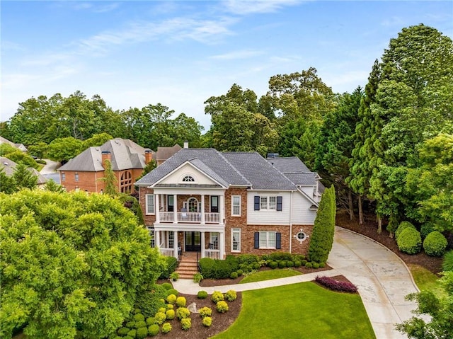 5173 Brendlynn Dr, Suwanee, GA 30024 - greek revival house with covered porch, brick siding, a balcony, a front lawn, and view of scattered trees