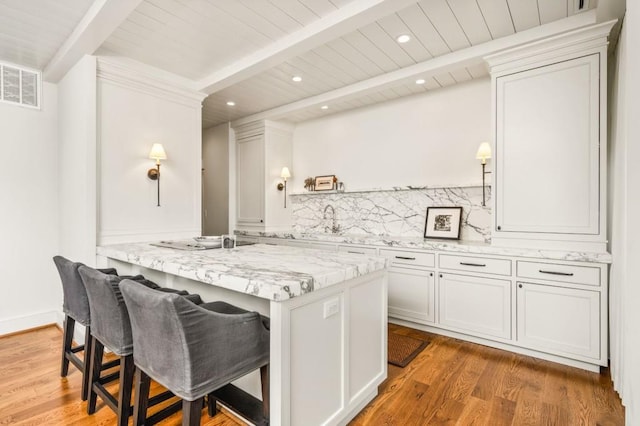 2575 Peachtree Rd NE Unit 8D, Atlanta, GA 30305 - kitchen featuring wooden ceiling with exposed beams, backsplash, wood finished floors, a kitchen bar, and light stone counters
