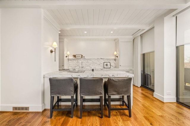 kitchen featuring a breakfast bar area, visible vents, white cabinetry, tasteful backsplash, and beamed ceiling