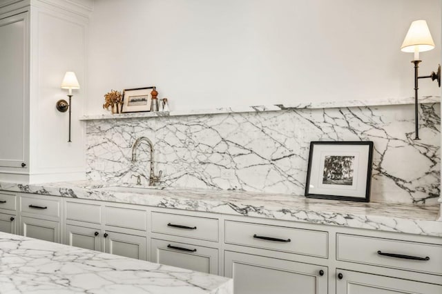 kitchen featuring light stone counters, white cabinetry, a sink, and decorative backsplash