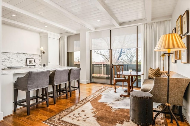 interior space featuring tasteful backsplash, a kitchen breakfast bar, beamed ceiling, wood finished floors, and a wall of windows