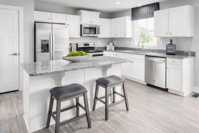 kitchen with a breakfast bar area, a sink, stainless steel appliances, white cabinets, and a center island