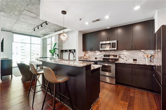 kitchen with stainless steel appliances, a kitchen breakfast bar, backsplash, light stone countertops, and dark wood-style floors