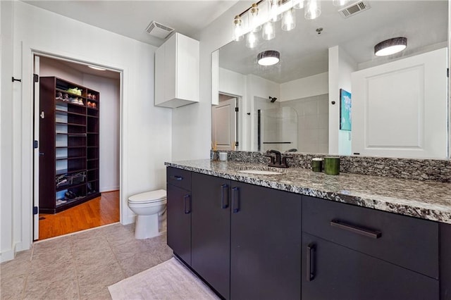 full bath featuring toilet, vanity, a tile shower, and visible vents