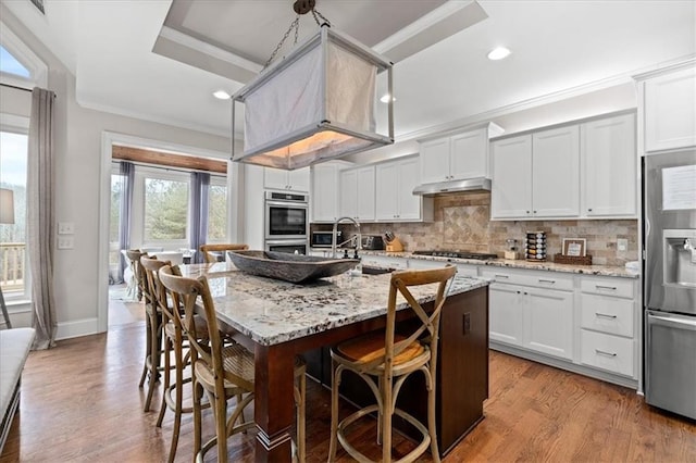 kitchen with an island with sink, white cabinetry, ornamental molding, and light hardwood / wood-style floors