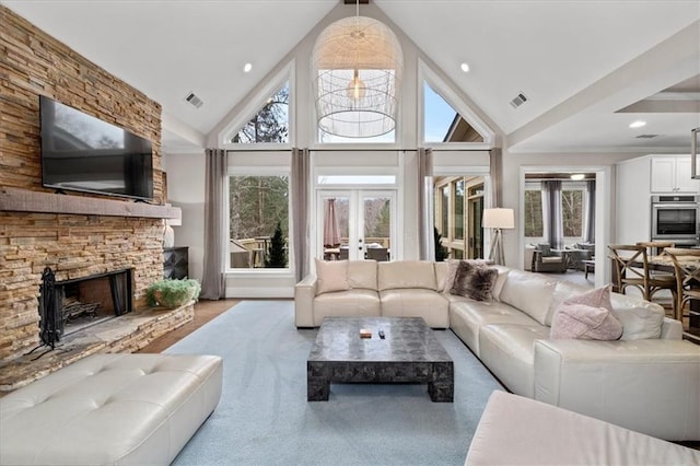 living room with a healthy amount of sunlight, high vaulted ceiling, a stone fireplace, and french doors