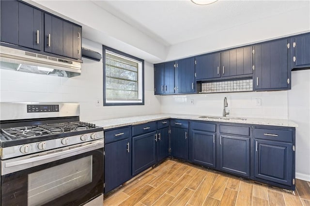 kitchen featuring under cabinet range hood, blue cabinetry, stainless steel range with gas cooktop, and a sink