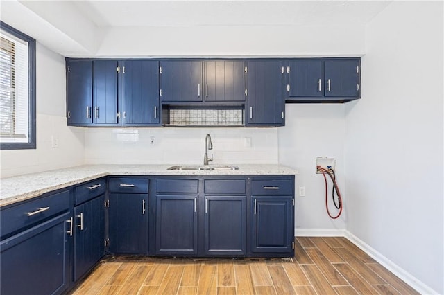 kitchen with decorative backsplash, wood finish floors, blue cabinetry, and a sink