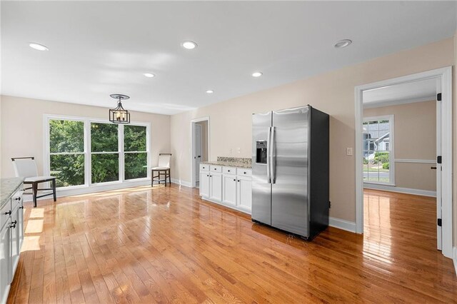 kitchen with light stone countertops, stainless steel fridge, white cabinetry, and hanging light fixtures