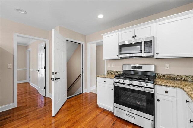 kitchen with dark stone countertops, white cabinetry, light hardwood / wood-style flooring, and stainless steel appliances