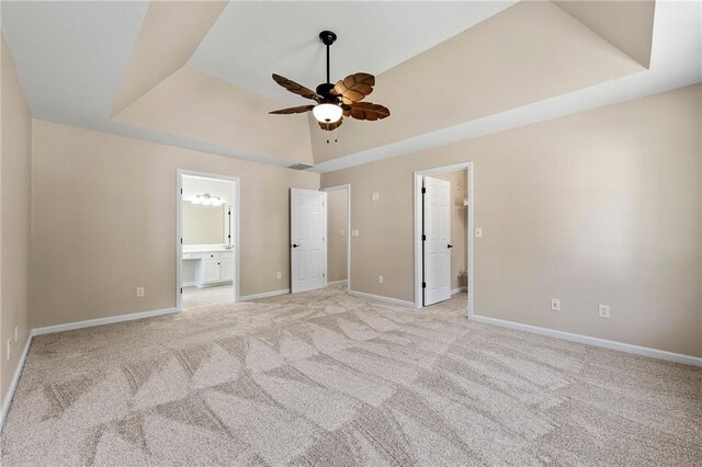 unfurnished bedroom with a tray ceiling, ensuite bathroom, ceiling fan, and light colored carpet