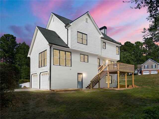 back house at dusk featuring a garage, a yard, and a wooden deck