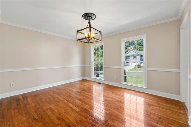 empty room with crown molding, wood-type flooring, and an inviting chandelier