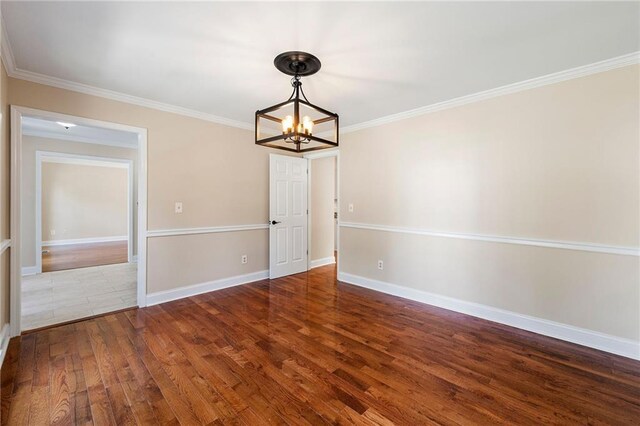 empty room with hardwood / wood-style flooring, ornamental molding, and an inviting chandelier