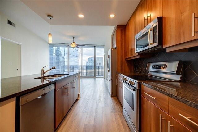 kitchen featuring decorative light fixtures, stainless steel appliances, decorative backsplash, dark stone countertops, and sink