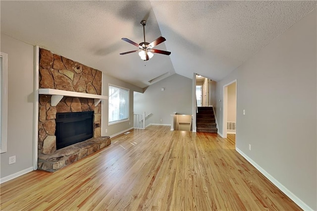 unfurnished living room featuring ceiling fan, light hardwood / wood-style floors, a textured ceiling, a stone fireplace, and vaulted ceiling