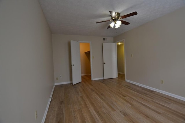 unfurnished bedroom with light hardwood / wood-style flooring, ceiling fan, a textured ceiling, a walk in closet, and a closet