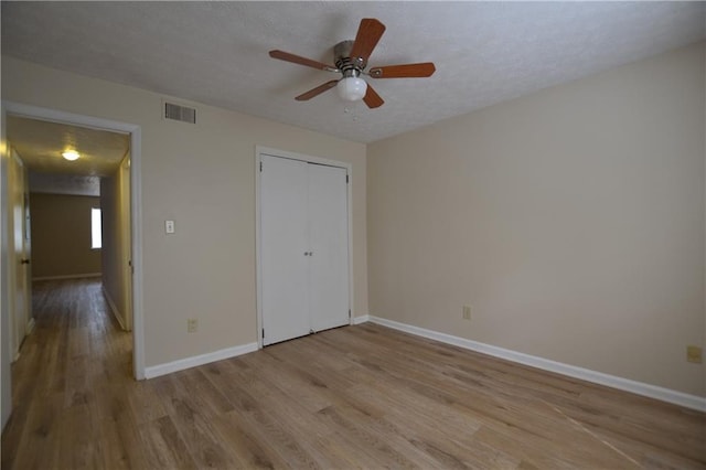 unfurnished bedroom with ceiling fan, a closet, a textured ceiling, and light wood-type flooring